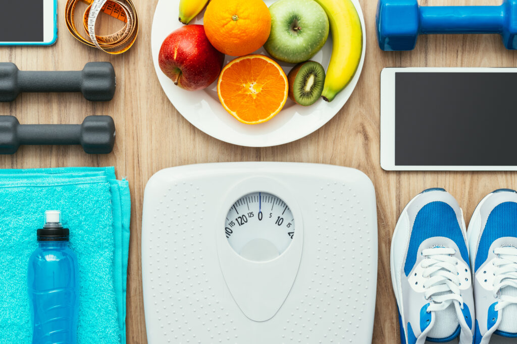 overhead shot of weight scale, water bottle, running shoes, fruit, and dumbells